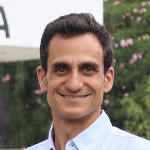 Joseadrián sonriendo, con camisa azul claro, frente a un muro con flores